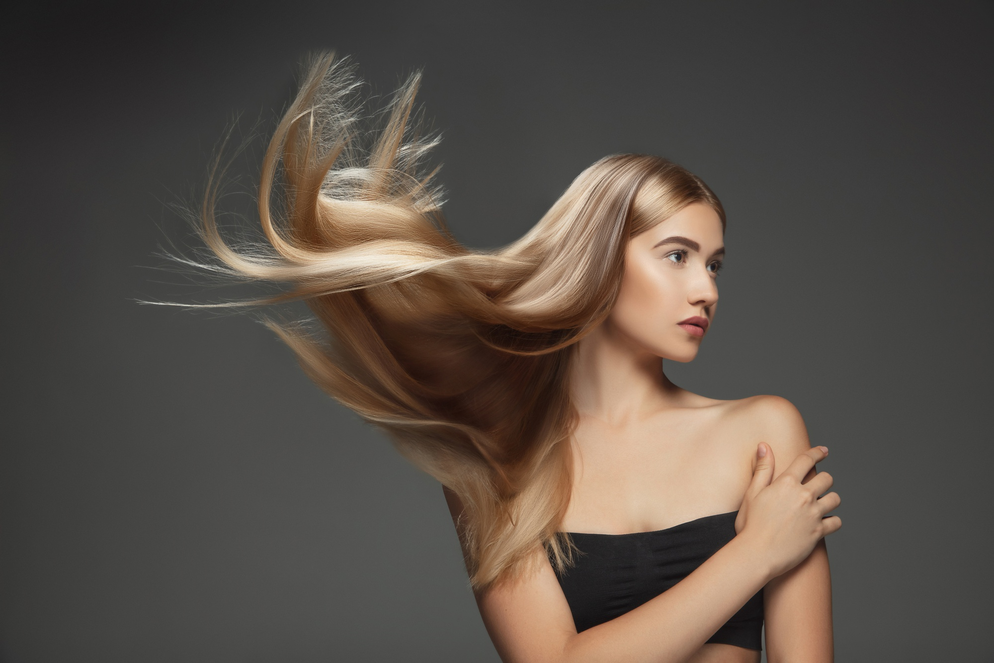 model-with-long-smooth-flying-blonde-hair-isolated-dark-grey-studio-background-young-caucasian-model-with-well-kept-skin-hair-blowing